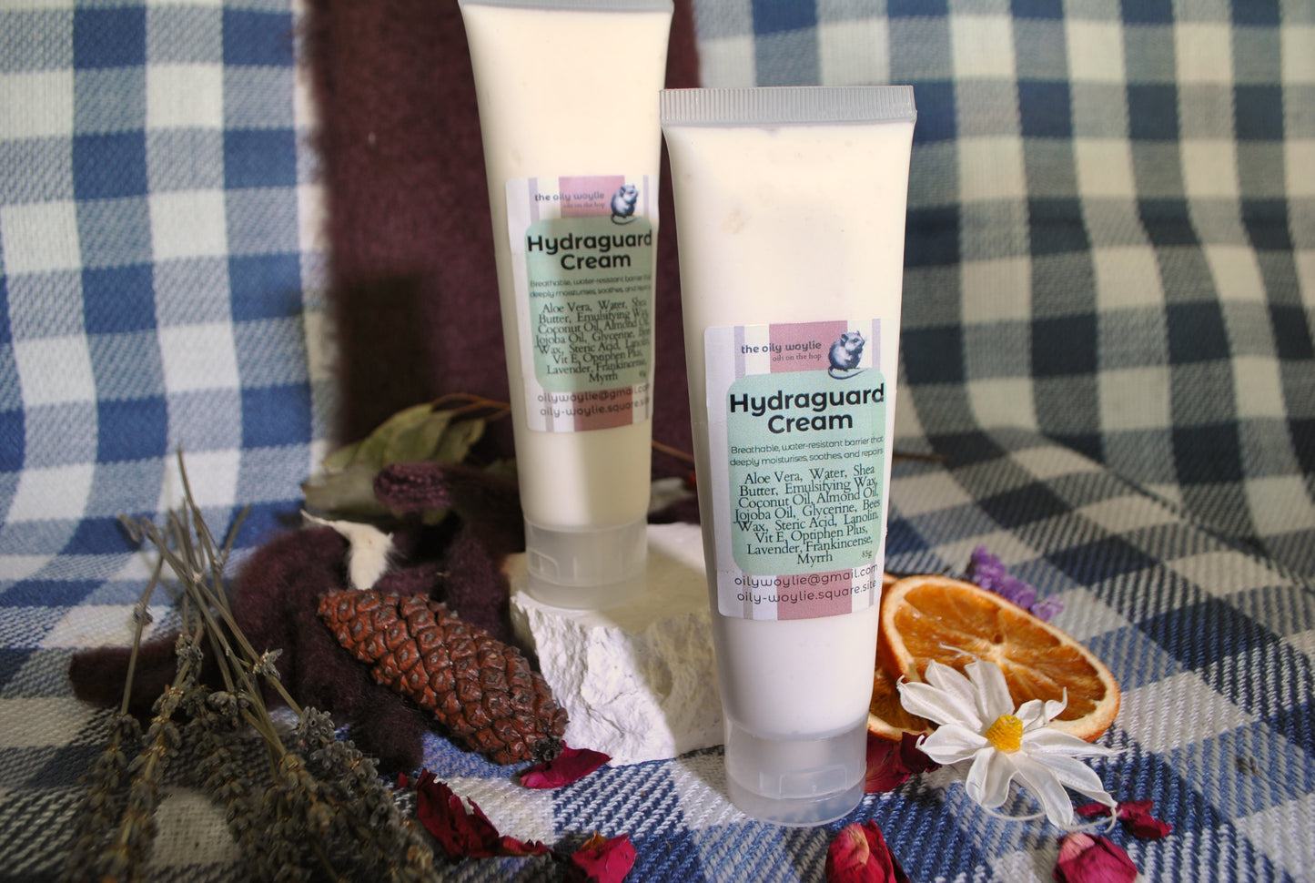 Hydraguard Cream tube, natural moisturising cream for dry skin protection on a checkered fabric background with flowers and leaves.