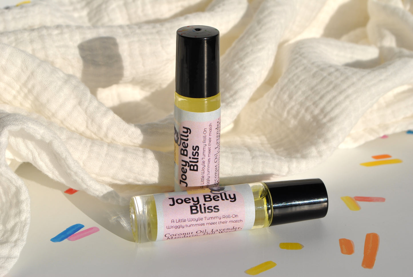 Joey Belly Bliss essential oil blend in a roller bottle, natural tummy support for kids on confetti background
