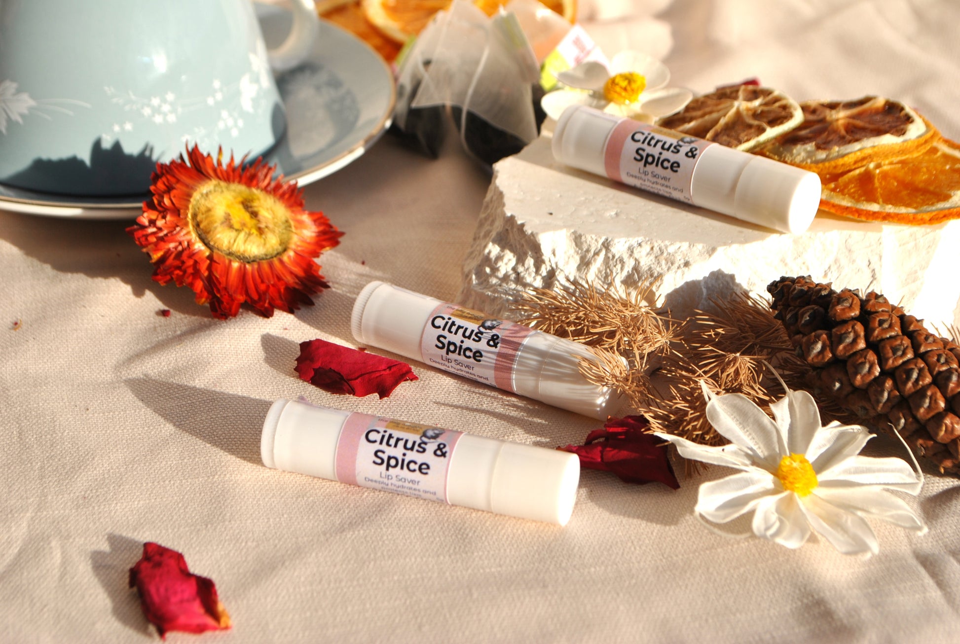Lip Saver Citrus & Spice balm stick, natural lip care on a table with flowers and a teacup.