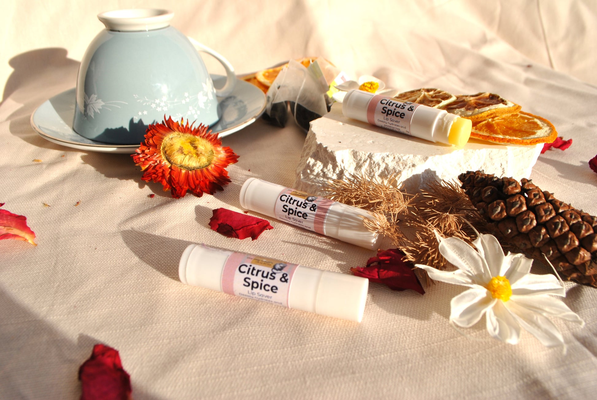 Lip Saver Citrus & Spice balm stick, natural lip care on a textured surface with flowers and a tea cup.