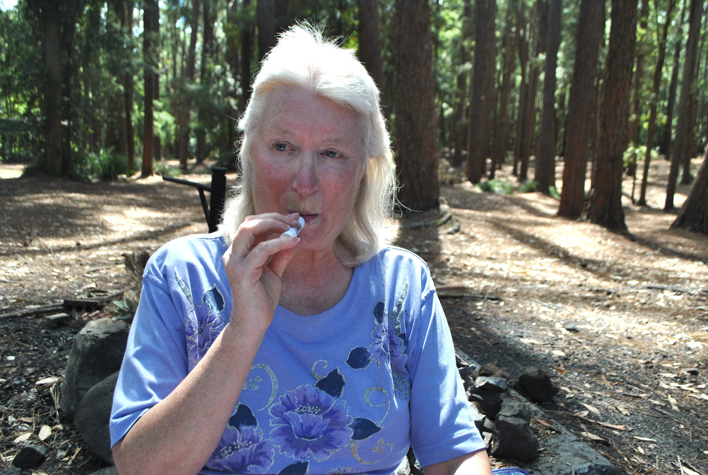 Person sitting cross-legged on a blue check picnic blanket in the Watagan Mountains, gently applying The Oily Woylie Lip Saver — natural hydration for dry lips.