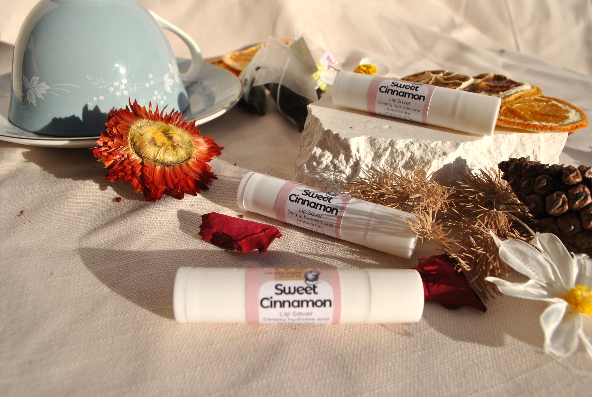 Lip Saver Sweet Cinnamon balm stick, natural lip care on a textured surface with flowers and a teacup.