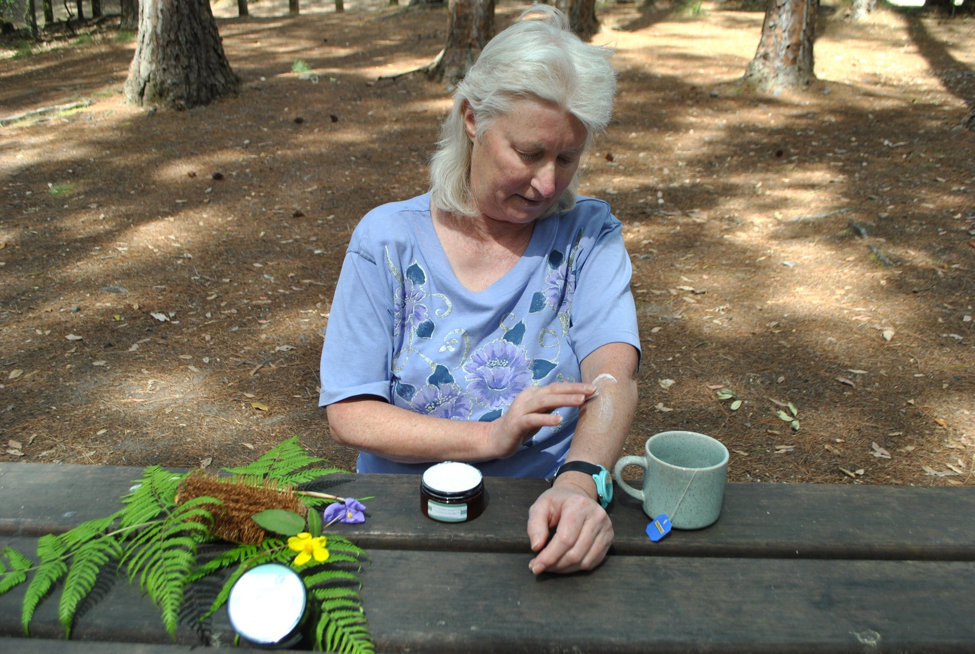 Close-up of hands massaging The Oily Woylie Magic Pain Cream into the arm while resting in the Australian bush — soothing botanical balm for aches and tension.