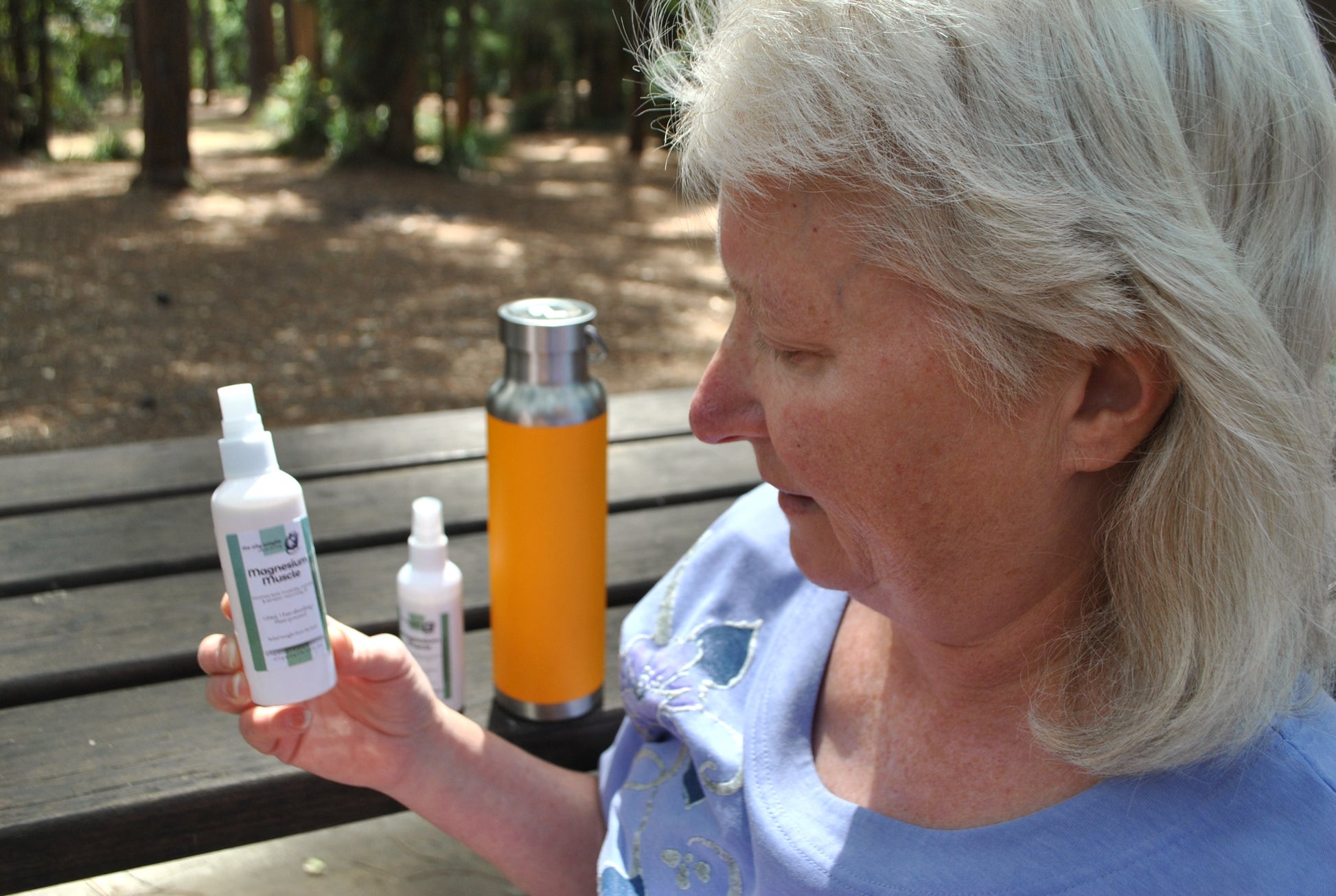 Person sitting at a picnic table in the Australian bush, applying The Oily Woylie Magnesium Muscle Spray to their leg after a walk — natural muscle recovery and relaxation.