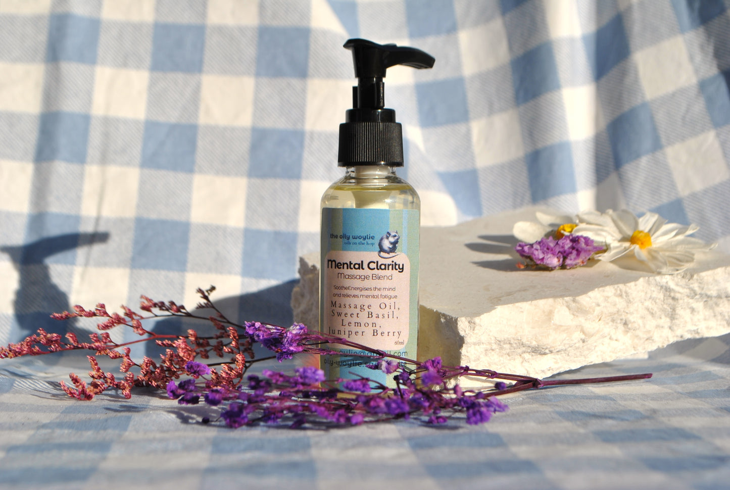 Mental Clarity Massage essential oil blend bottle, natural support for focus and concentration on a checkered fabric background with flowers.