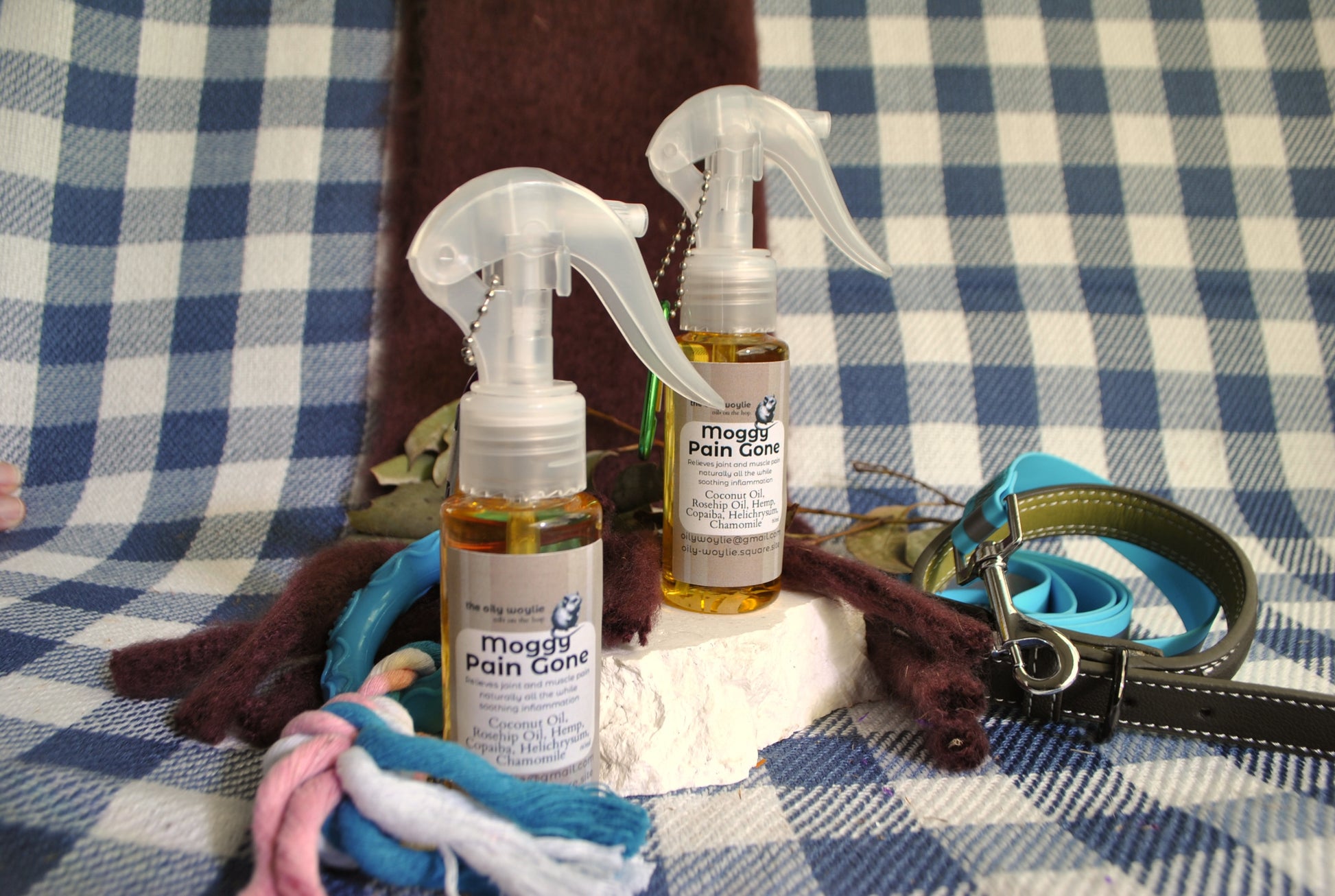 Moggy Pain Gone spray bottle, natural relief spray for cats with sore muscles and joints on a checkered fabric background with pet accessories.