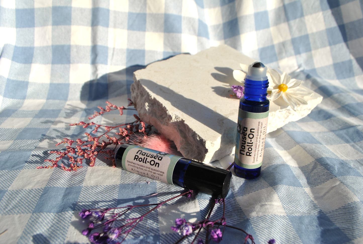 Nausea Roll essential oil roller blend, natural support for nausea and upset stomach on a checkered fabric background with flowers.