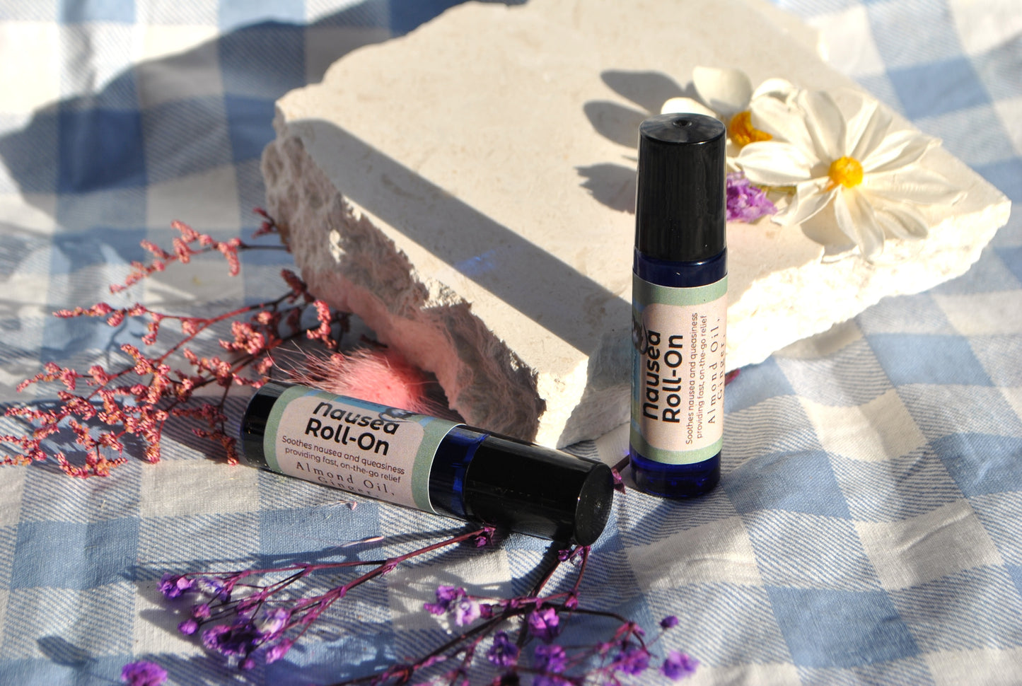Nausea Roll essential oil roller blend, natural support for nausea and upset stomach on a checkered fabric background with flowers.