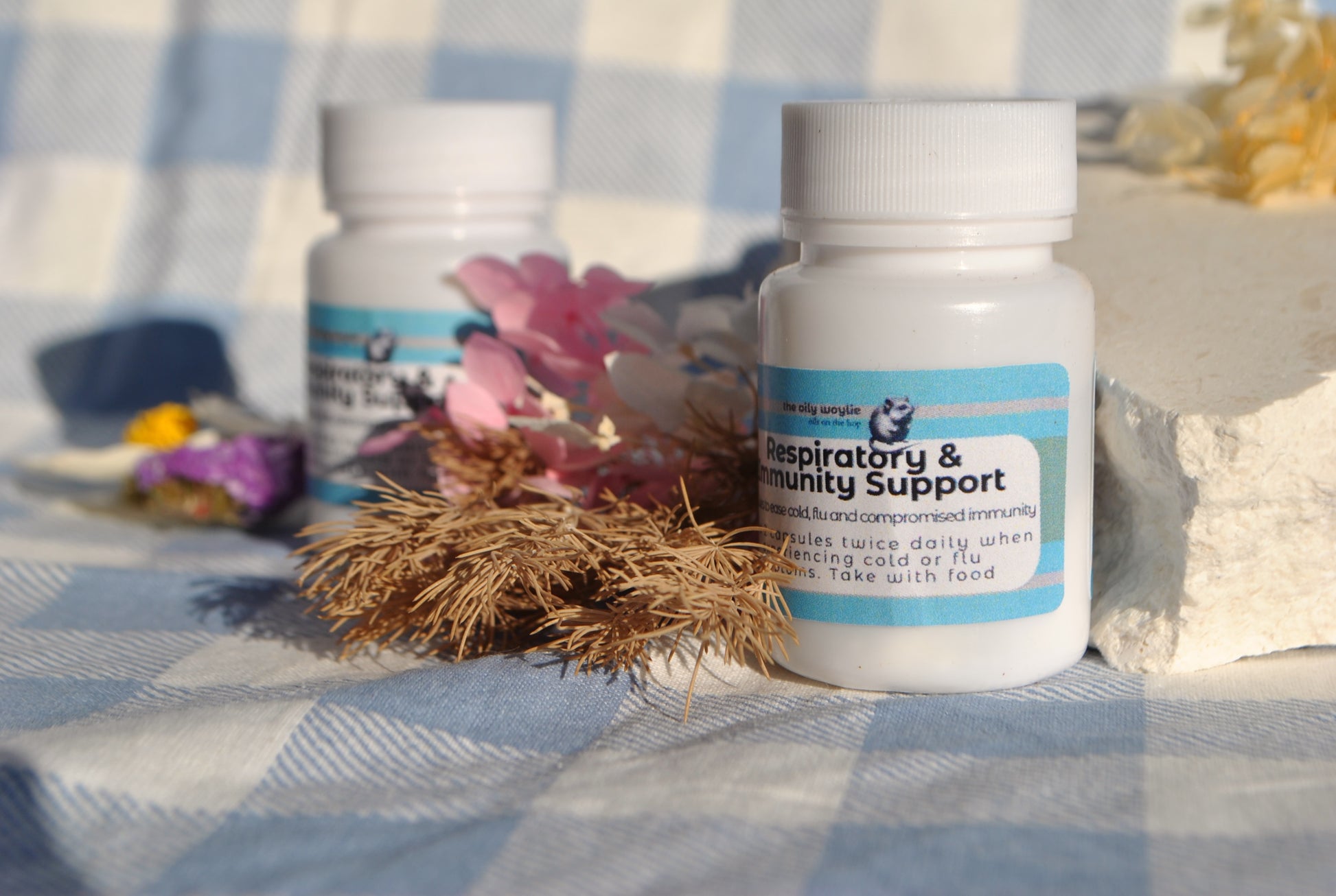 Respiratory & Immune Support Capsules bottle, natural supplement to support breathing and immunity on a checkered fabric background with flowers and herbs.