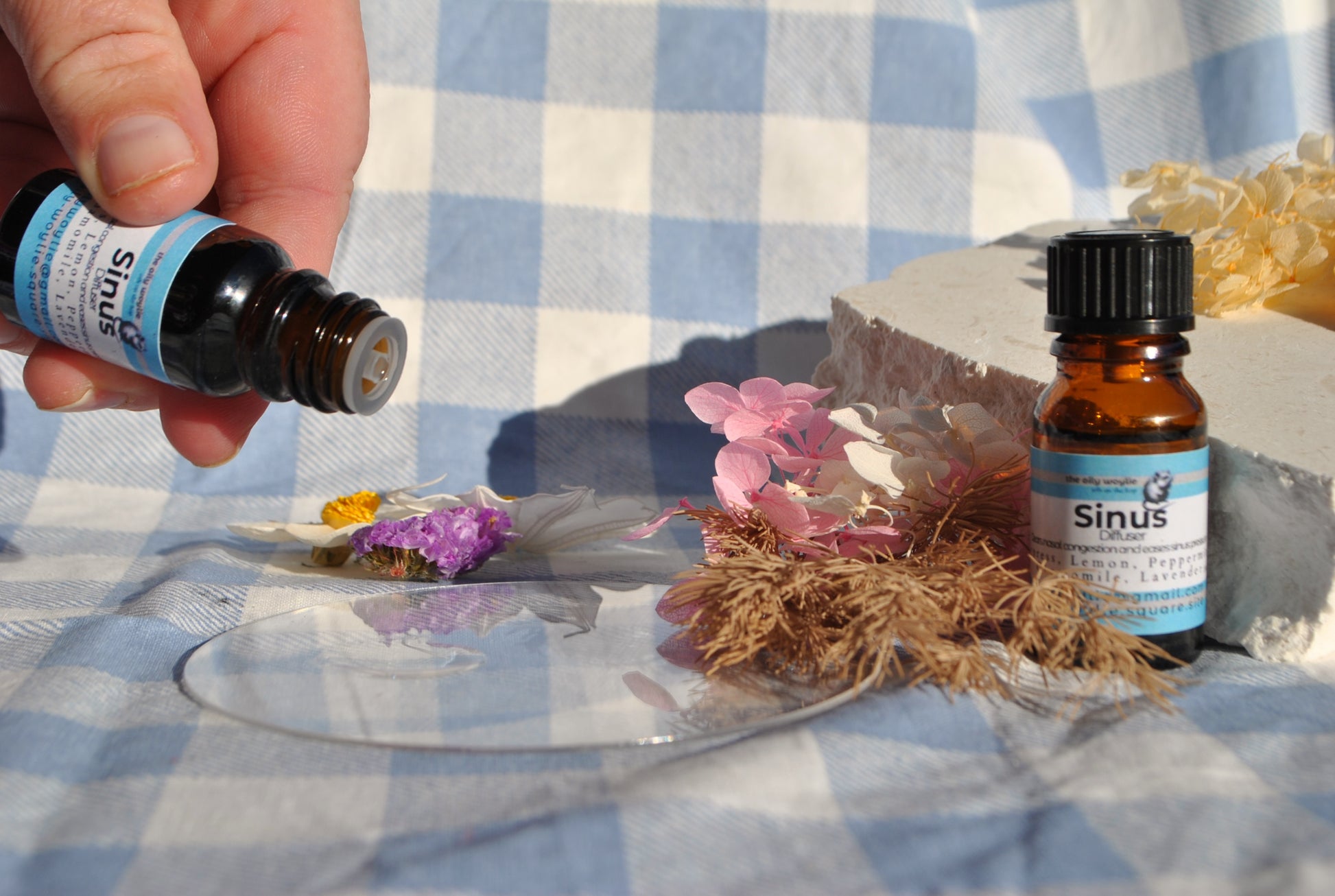 Sinus Diffuser Blend essential oil bottle, natural blend for sinus relief and clear breathing on a checkered tablecloth with flowers and hay.