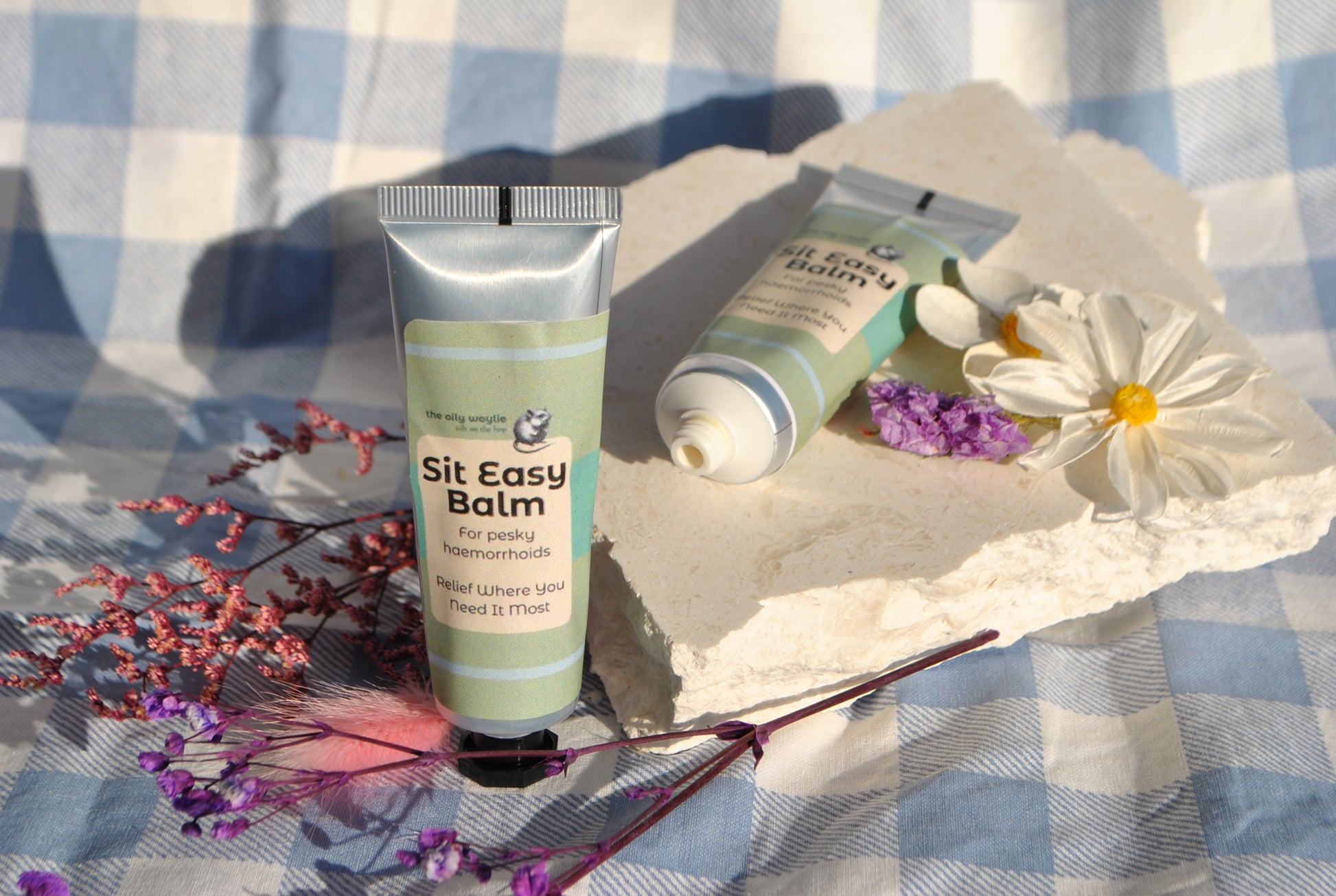 Sit Easy Balm tube, natural soothing balm for haemorrhoid discomfort on a checkered fabric background with flowers.