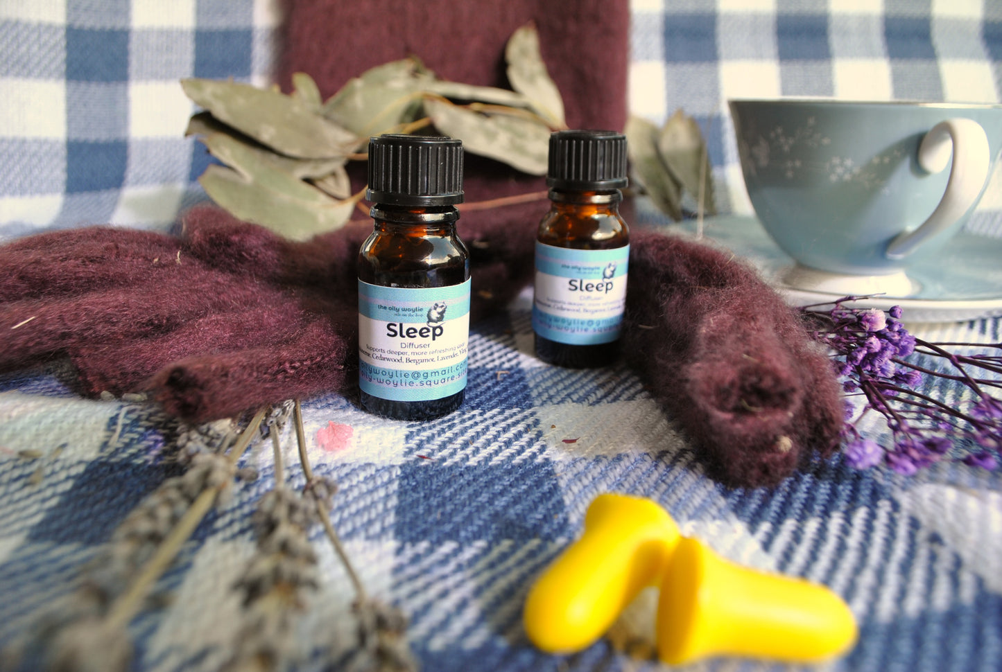 Sleep Diffuser Blend essential oil bottle, natural calming blend for restful sleep on a checkered fabric background with dried herbs and a tea cup.