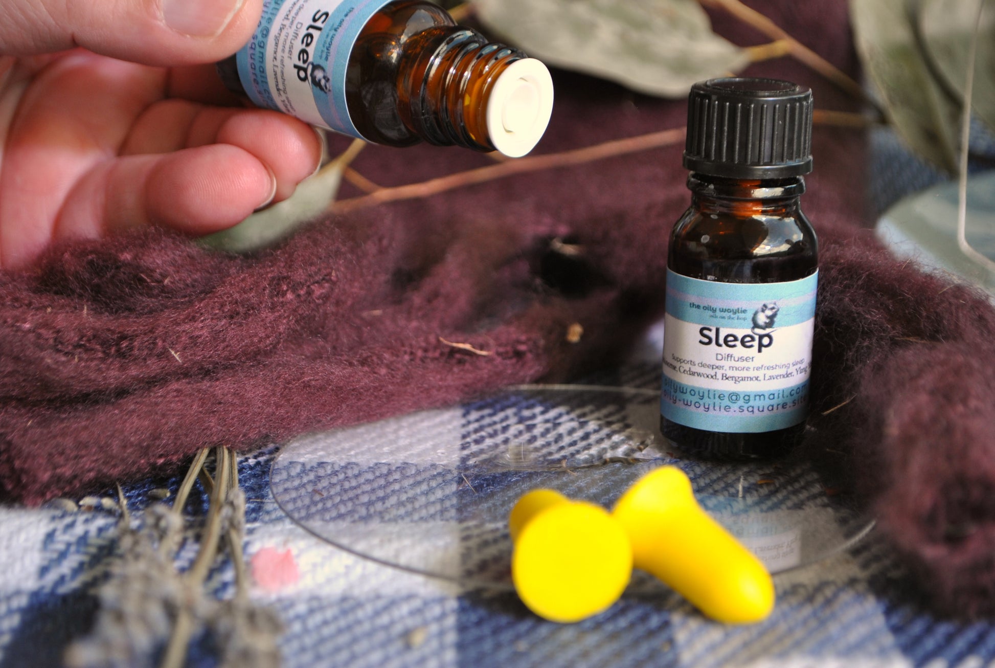 Sleep Diffuser Blend essential oil bottle, natural calming blend for restful sleep on a checkered fabric with a yellow ear plugs nearby.