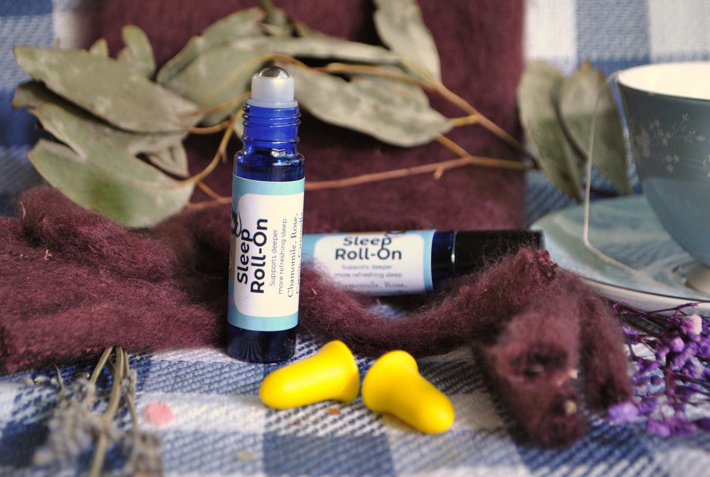 Sleep Roll essential oil roller blend, natural calming support for restful sleep with yellow earplugs on a checkered fabric background