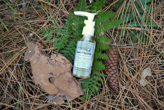 Sore Muscle Massage essential oil blend bottle, natural support for muscle aches and recovery, natural background with leaves and pine cones.
