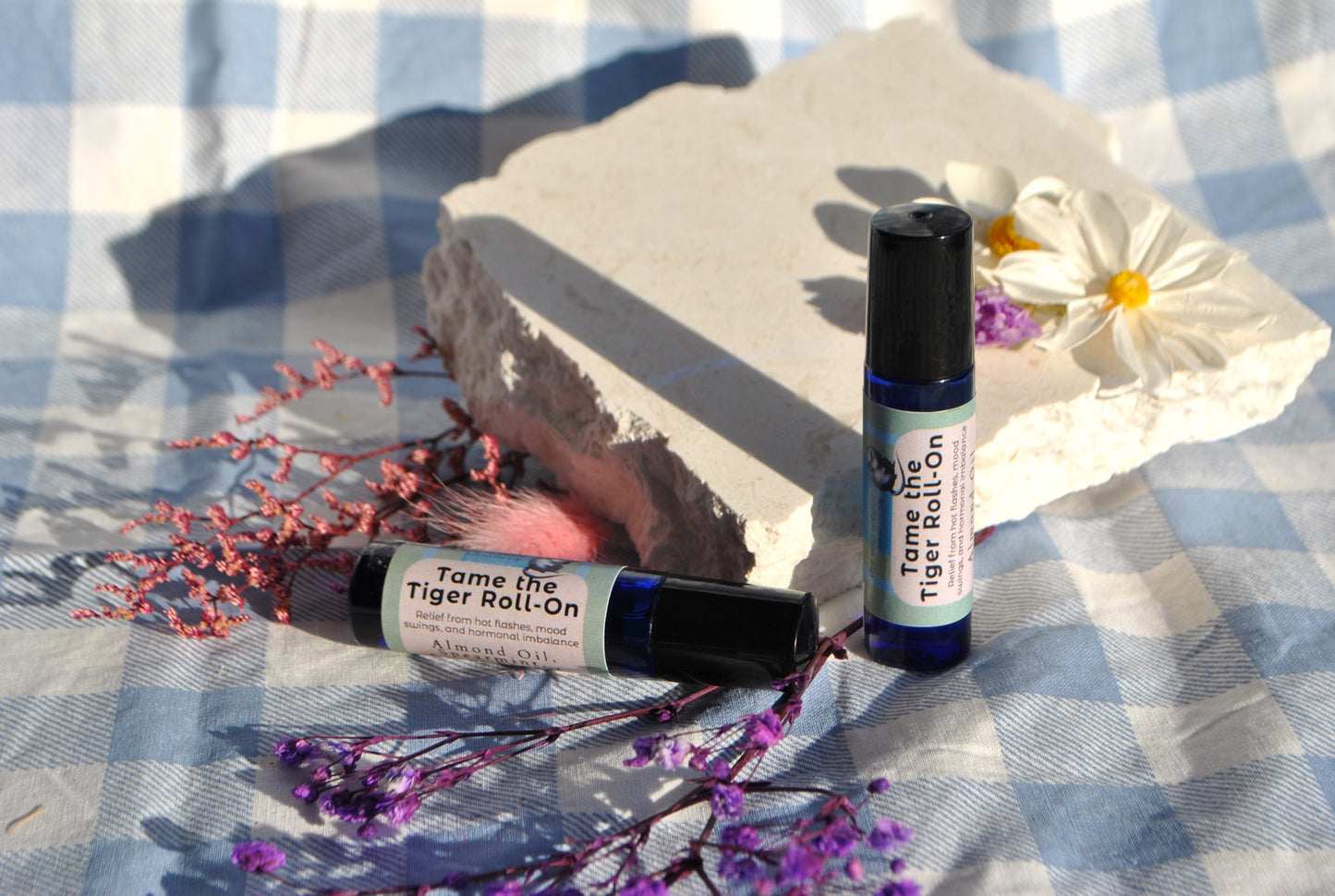 Tame the Tiger Roll essential oil roller blend, natural support for hormones and mood on a checkered fabric background with flowers and rocks.