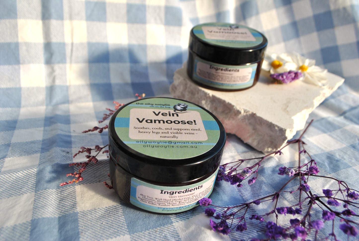 Vein Vamoose natural gel jar, cooling cream to support healthy circulation on a checkered fabric background with flowers.