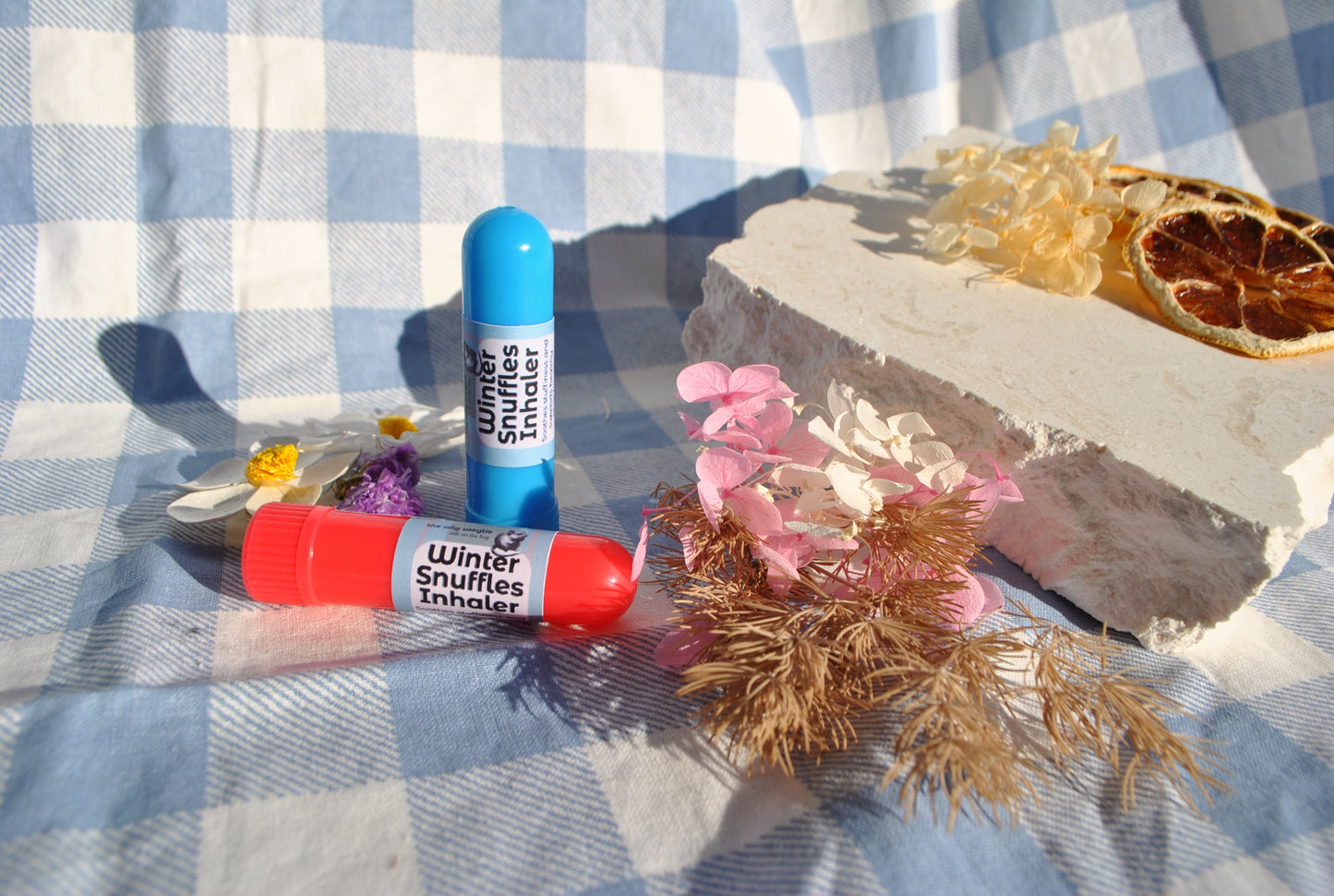 Winter Snuffles Inhaler tube, natural essential oil inhaler for colds and congestion on a checkered tablecloth with flowers and a rock.