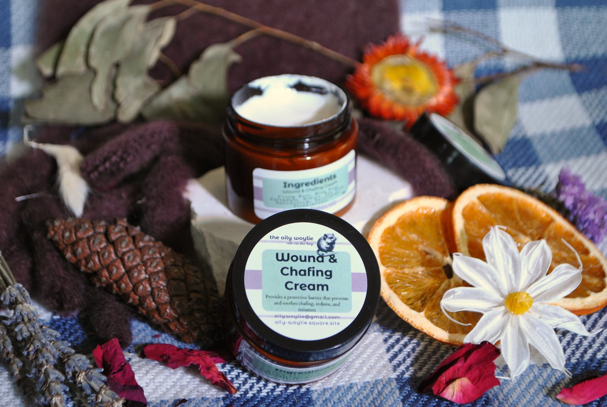 Wound & Chafing Cream jar, natural cream to soothe skin irritation and chafing on a checkered fabric background with flowers and oranges.