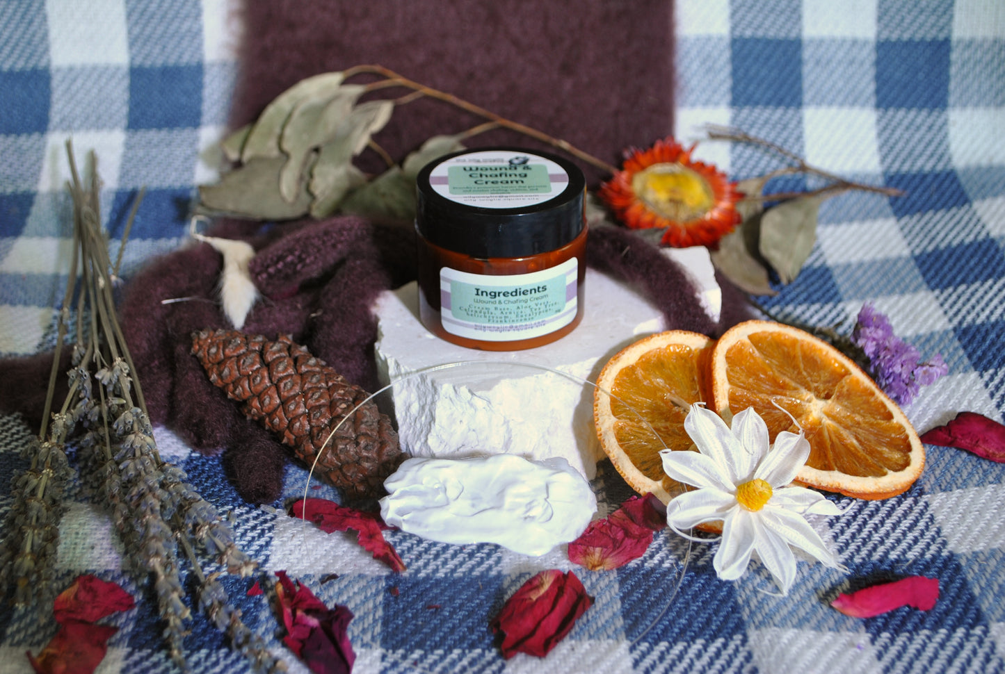 Wound & Chafing Cream jar, natural cream to soothe skin irritation and chafing on a checkered cloth with flowers and oranges