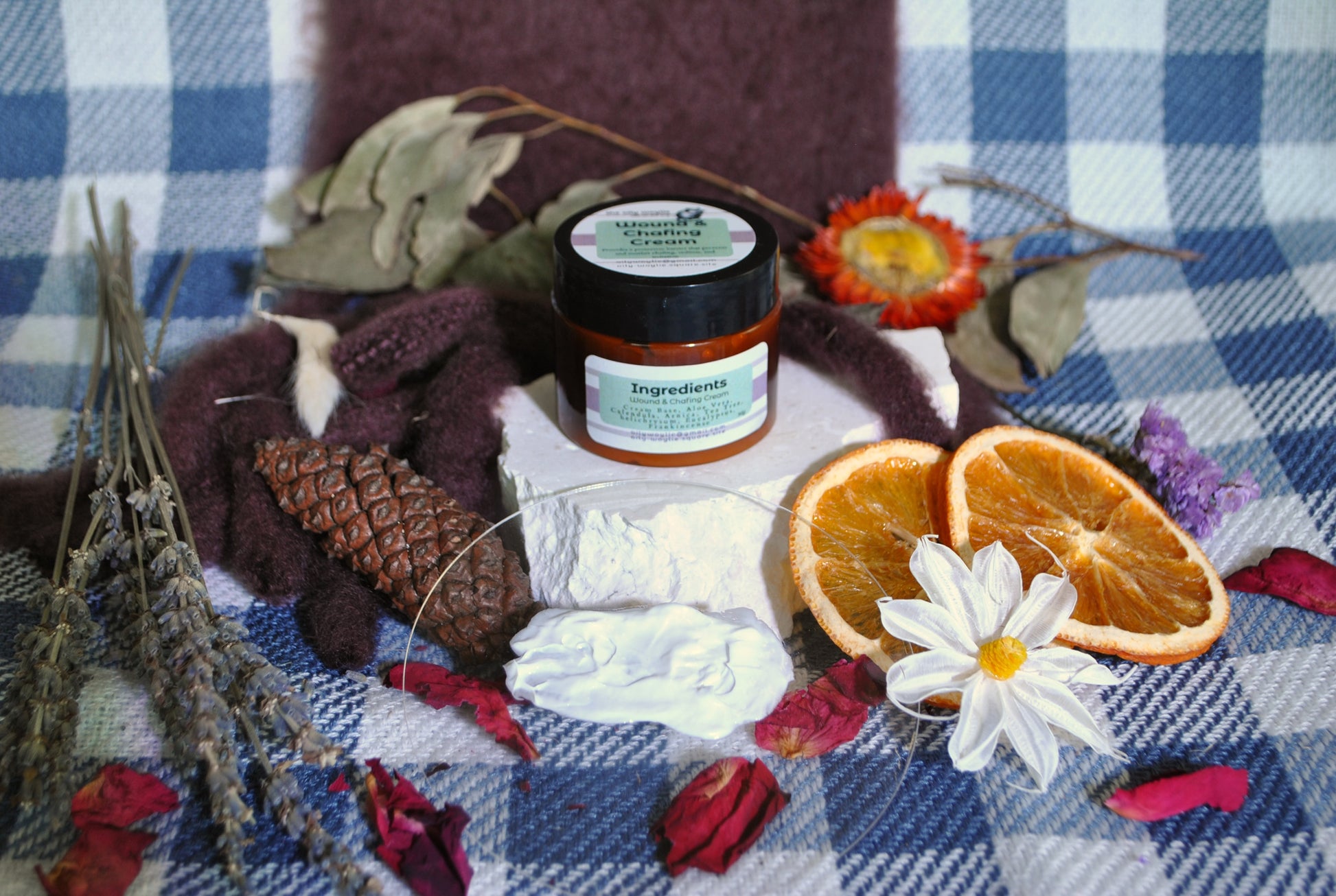 Wound & Chafing Cream jar, natural cream to soothe skin irritation and chafing on a checkered cloth with flowers and oranges